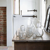 Sir Madam hand-blown seeded glass carafe and drinking glass set with organic shapes on a rustic wooden table.