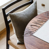 Glenmore Woven Dining Chair in smoked oak with a paper cord seat and olive linen pillow at a walnut table