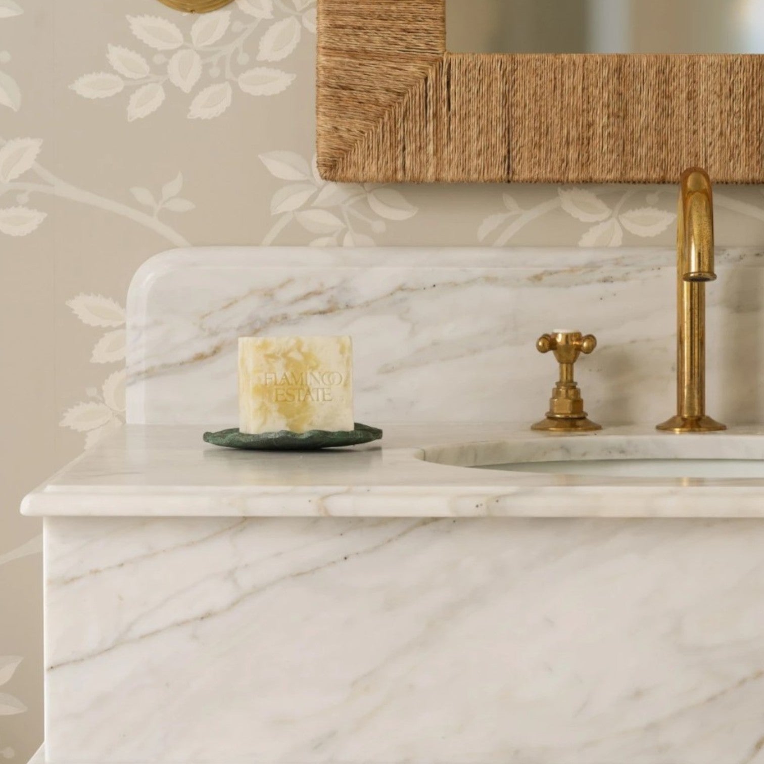 Calimia Home Golden Pollinator soap brick on a green dish, set on a white marble vanity with a brass faucet.
