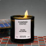 Flamingo Estate Golden Pollinator scented candle in a dark glass jar with a lit wick on a tiled surface.