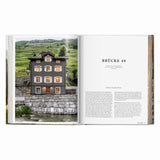 Calimia Home Great Escapes Alps book open to the Brücke 49 spread showing a historic stone guesthouse in Vals.