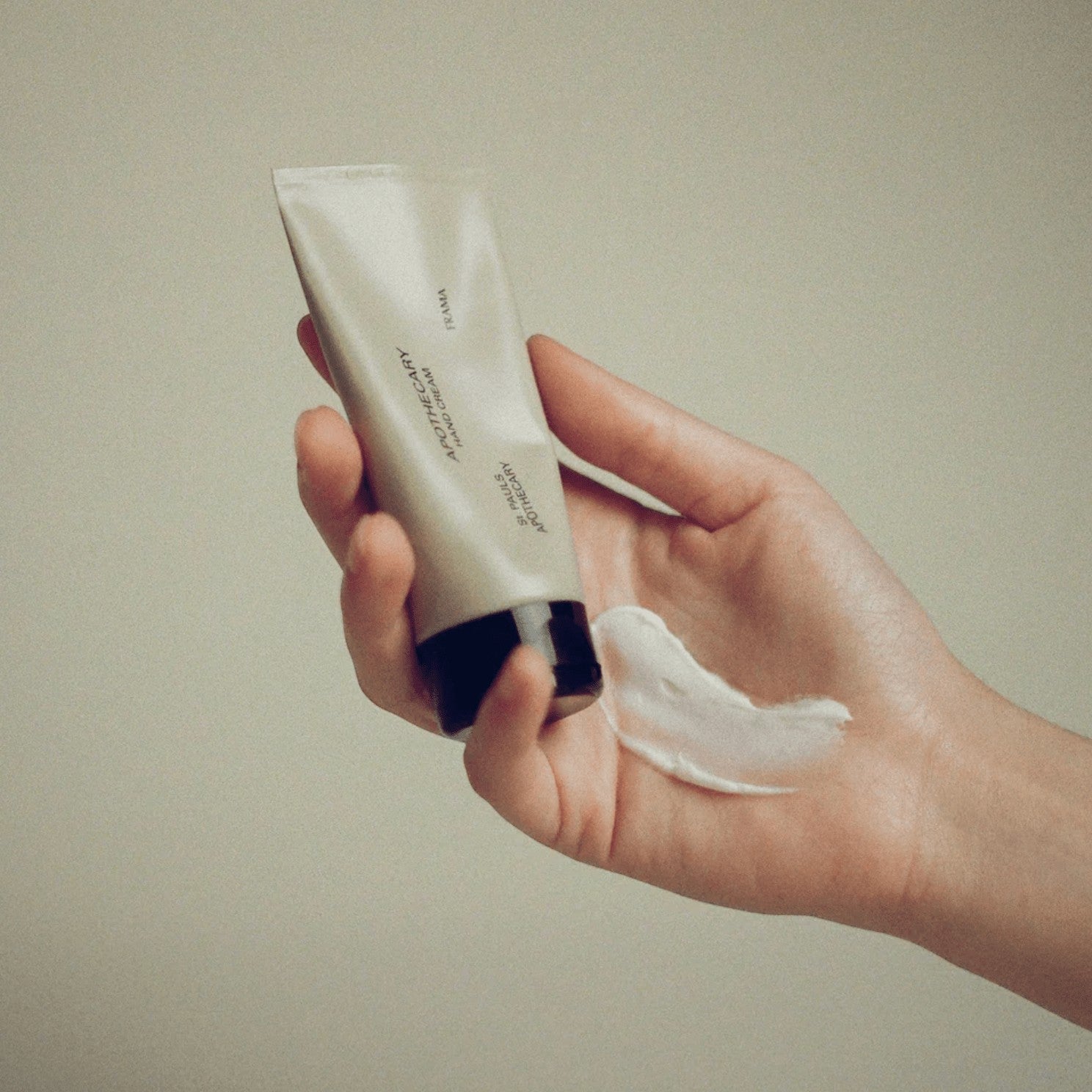 Frama Apothecary hand cream in a beige tube held in a hand with a dollop of white nourishing cream
