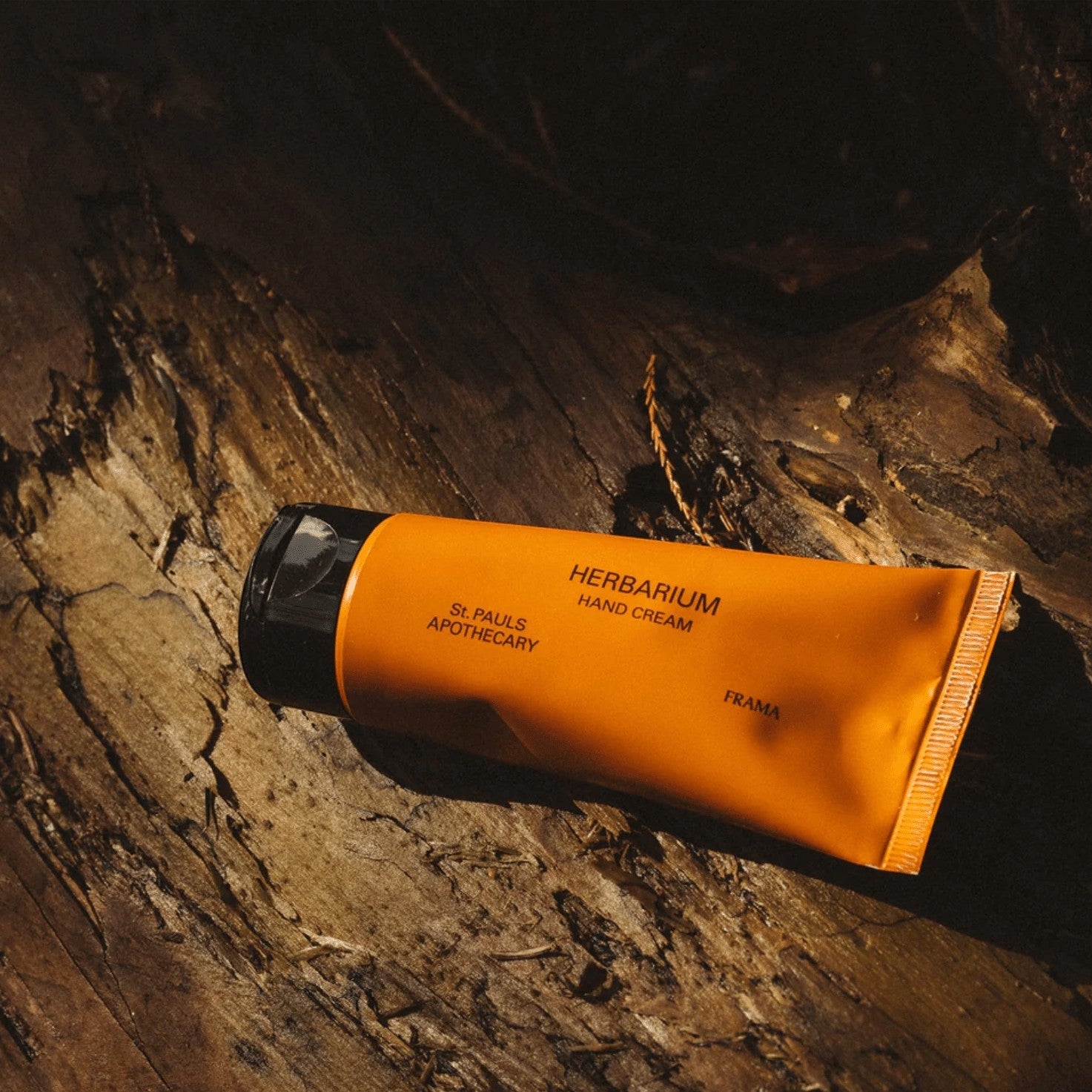 Frama Herbarium hand cream in an orange tube resting on textured dark wood bark.
