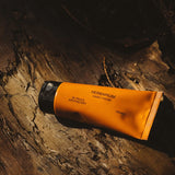 Frama Herbarium hand cream in an orange tube resting on textured dark wood bark.