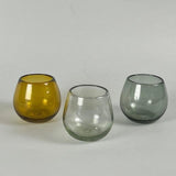 Calimia Home Roli Poli stemless glasses in amber, clear, and grey hand-blown recycled glass with a rounded shape.
