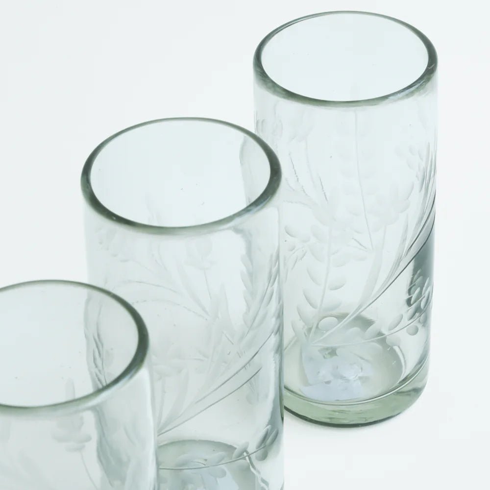 Three Handmade Etched Glass tumblers, featuring hand-etched leaf and branch designs and a slightly frosted finish, are arranged diagonally on a white background. The glasses are empty.
