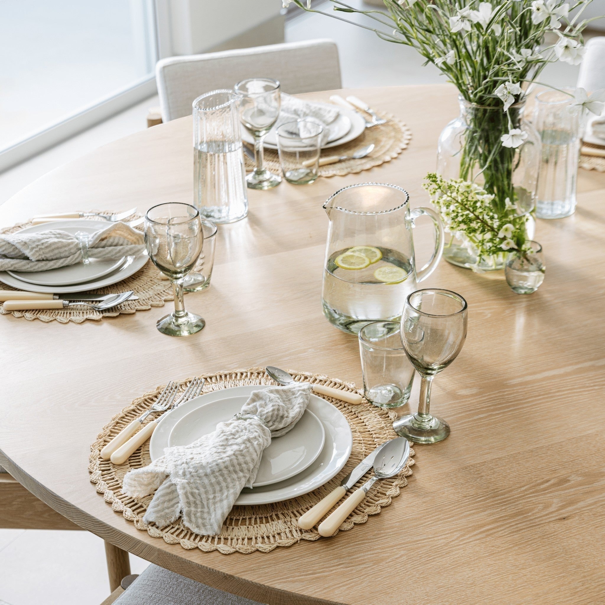 Pom Pom At Home Healdsburg Napkins in ocean blue with thin stripes and fringe edges set on a wooden dining table.