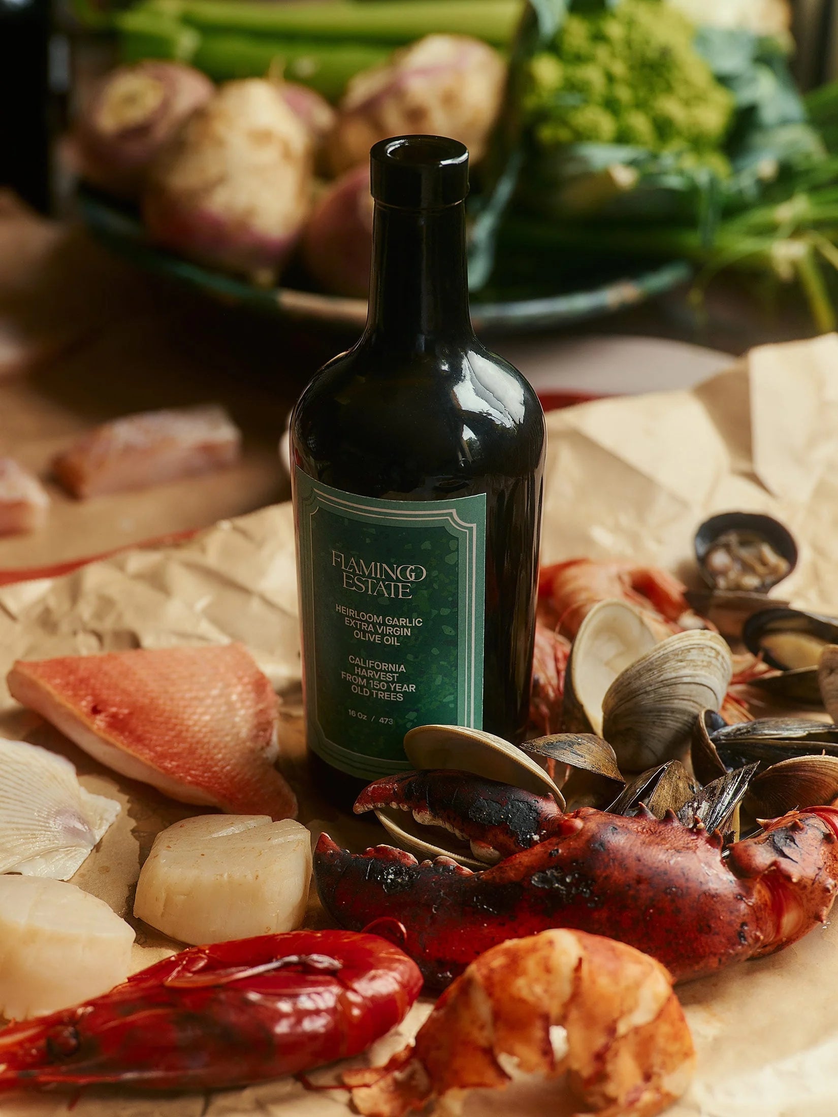 Flamingo Estate Heirloom Garlic olive oil sits on butcher paper amid raw lobster, shrimp, scallops, clams, and fish ready for the kitchen.