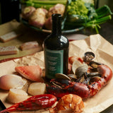 Flamingo Estate Heirloom Garlic olive oil sits on butcher paper amid raw lobster, shrimp, scallops, clams, and fish ready for the kitchen.