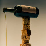 A dark Flamingo Estate Heritage olive oil bottle balances on a tower of bread cubes, golden oil dripping from its lip in a moody studio shot.