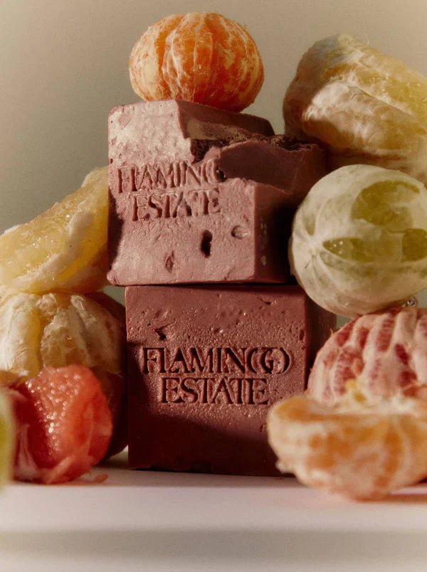 Stacked rose-pink Flamingo Estate Jasmine Damask Rose Soap Bricks surrounded by peeled tangerines, oranges and a halved grapefruit in a warm still life.