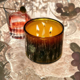 Flamingo Estate Jasmine Damask Rose XL three-wick candle in a dark amber glass vessel glowing on a textured tray