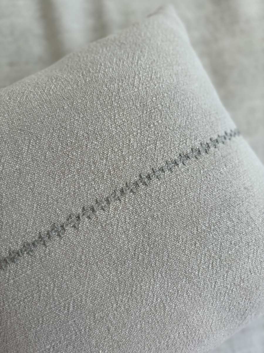 Close-up detail of the Lea Pillow showing the hand-embroidered line pattern on natural beige Belgian linen