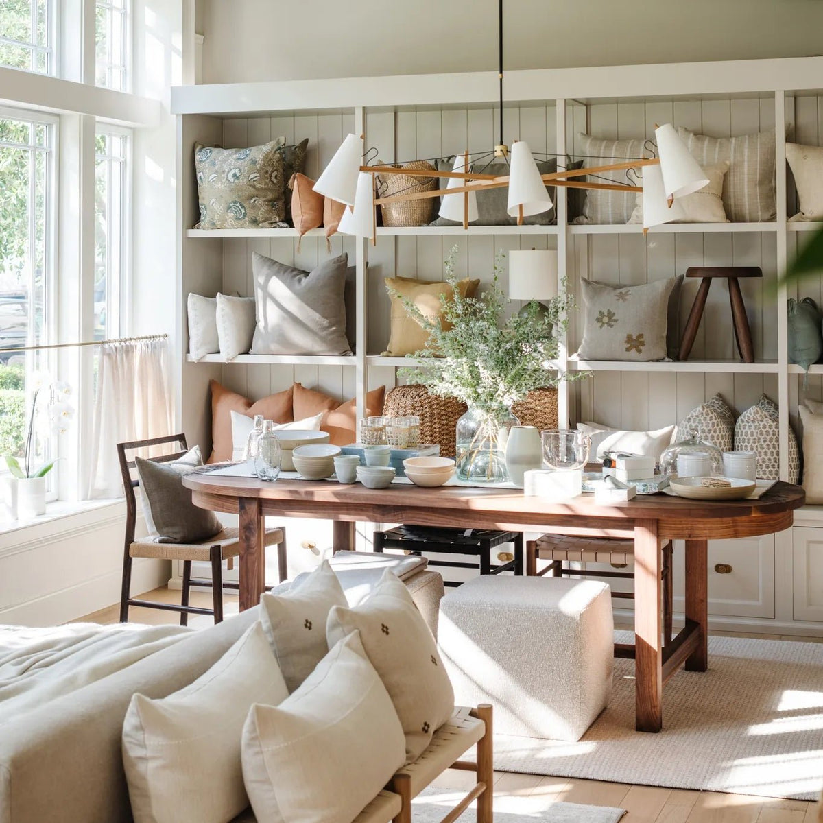 Long Hood Chandelier and pillow wall behind a woven oak bench with linen pillows at Calimia Home