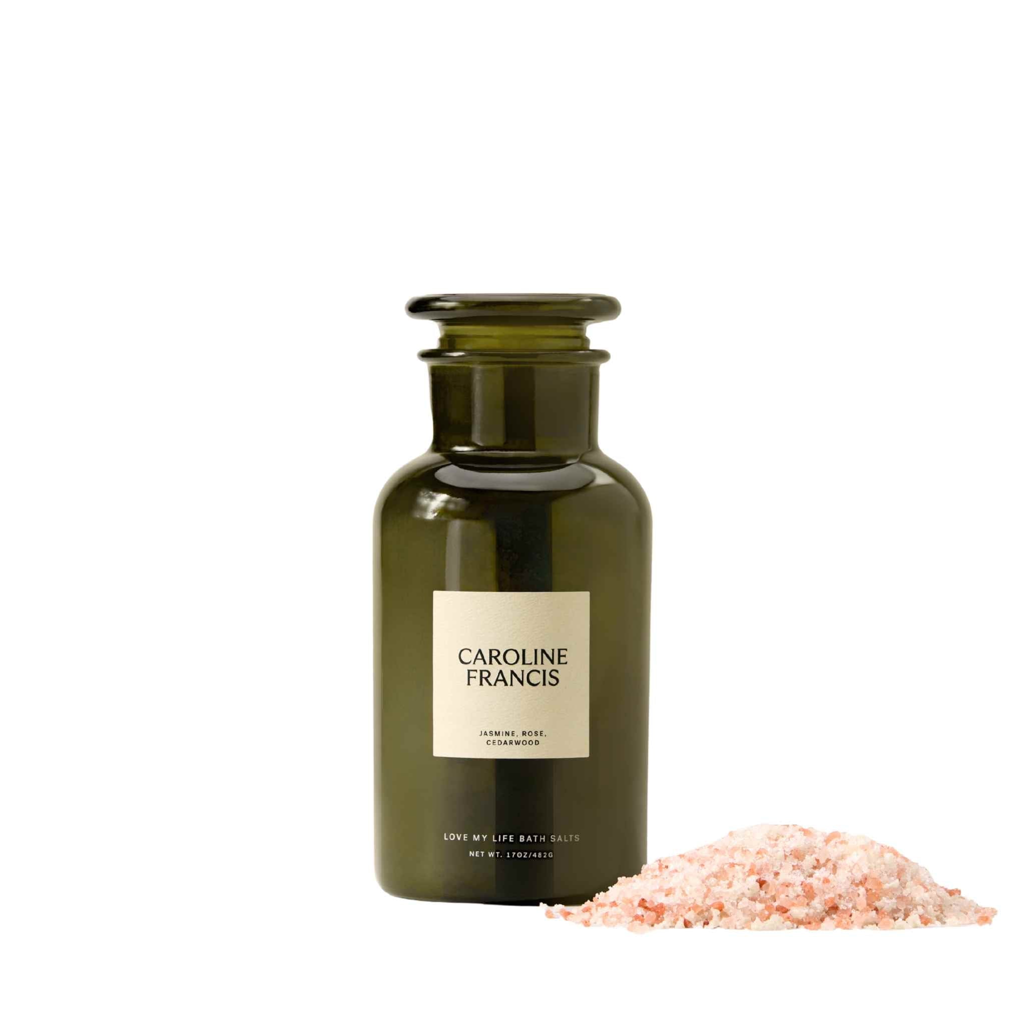Caroline Francis Love My Life Bath Salts in a green glass apothecary bottle next to a loose pile of pink Himalayan bath salts.