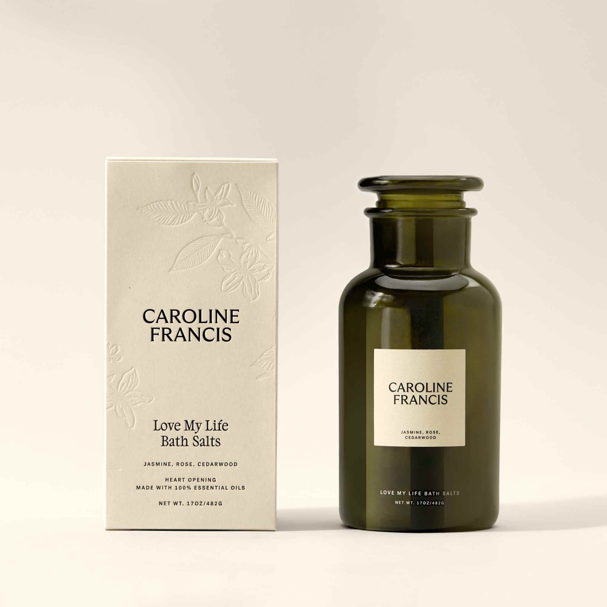 Caroline Francis Love My Life Bath Salts bottle beside its embossed cream box, which lists jasmine, rose, and cedarwood essential oils.