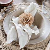 Talah Home natural straw flower napkin ring on a beige linen napkin in a ceramic bowl on a woven placemat