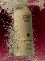 A cream Flamingo Estate Euphoria Body Wash bottle plunges through bubbling deep red water, sinking dramatically in a wine-toned bath.