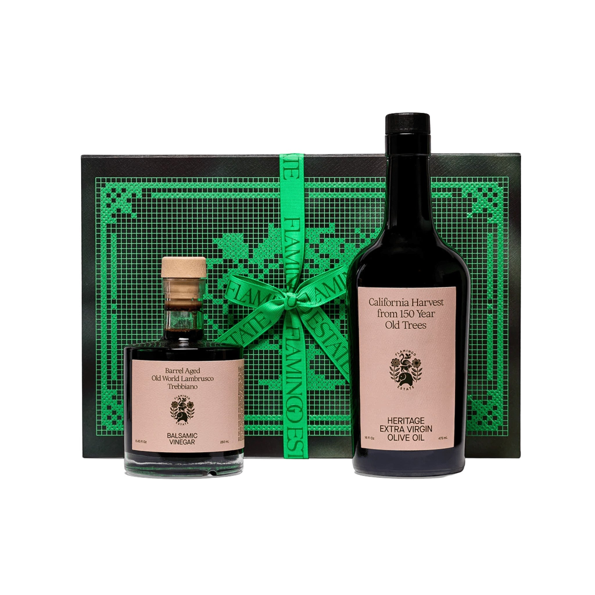 Flamingo Estate Tablemates Gift Set: a Heritage Extra Virgin Olive Oil bottle and Barrel Aged Balsamic Vinegar with cork stand before a black and green embroidered box tied with ribbon.
