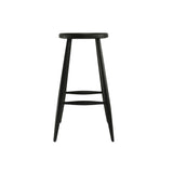 Calimia Home Omah stool in black stained wood with a round seat, tapered legs, and integrated footrests.