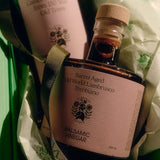 The Flamingo Estate Balsamic Vinegar bottle nests in green tissue and ribbon beside a Heritage olive oil, ready as a gift from Calimia Home Shop.