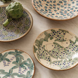 Calimia Home handcrafted ceramic plates featuring hand-painted palm, fish, and floral motifs on a marble surface.