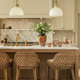 Calimia Home Rattan Cage Pitcher with handwoven seagrass wrap and glass body on a kitchen island with rattan stools