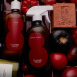 Flamingo Estate Roma Heirloom Tomato Lotion and Surface Cleaner bottles nestle among ripe red and dark heirloom tomatoes alongside a tomato soap bar.