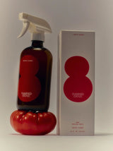A Flamingo Estate Roma Heirloom Tomato Surface Cleaner stands on a ripe red heirloom tomato beside its cream Limited Harvest box on a soft cream backdrop.