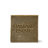 The olive-green Flamingo Estate Rosemary & Parsley Soap Brick, flecked with herbs and embossed with the brand wordmark, on a white background.