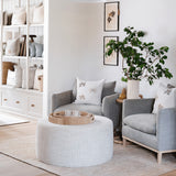 Calimia Home round ottoman upholstered in light beige Belgian linen, styled in a living room with grey armchairs.