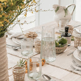 Be Home Ruffle Glass Lines Carafe with ribbed texture on a rustic dining table setting with glassware and fruit.