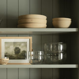 Be Home clear glass bowls with delicate ruffled rims stacked on a green shelf with rustic ceramic bowls