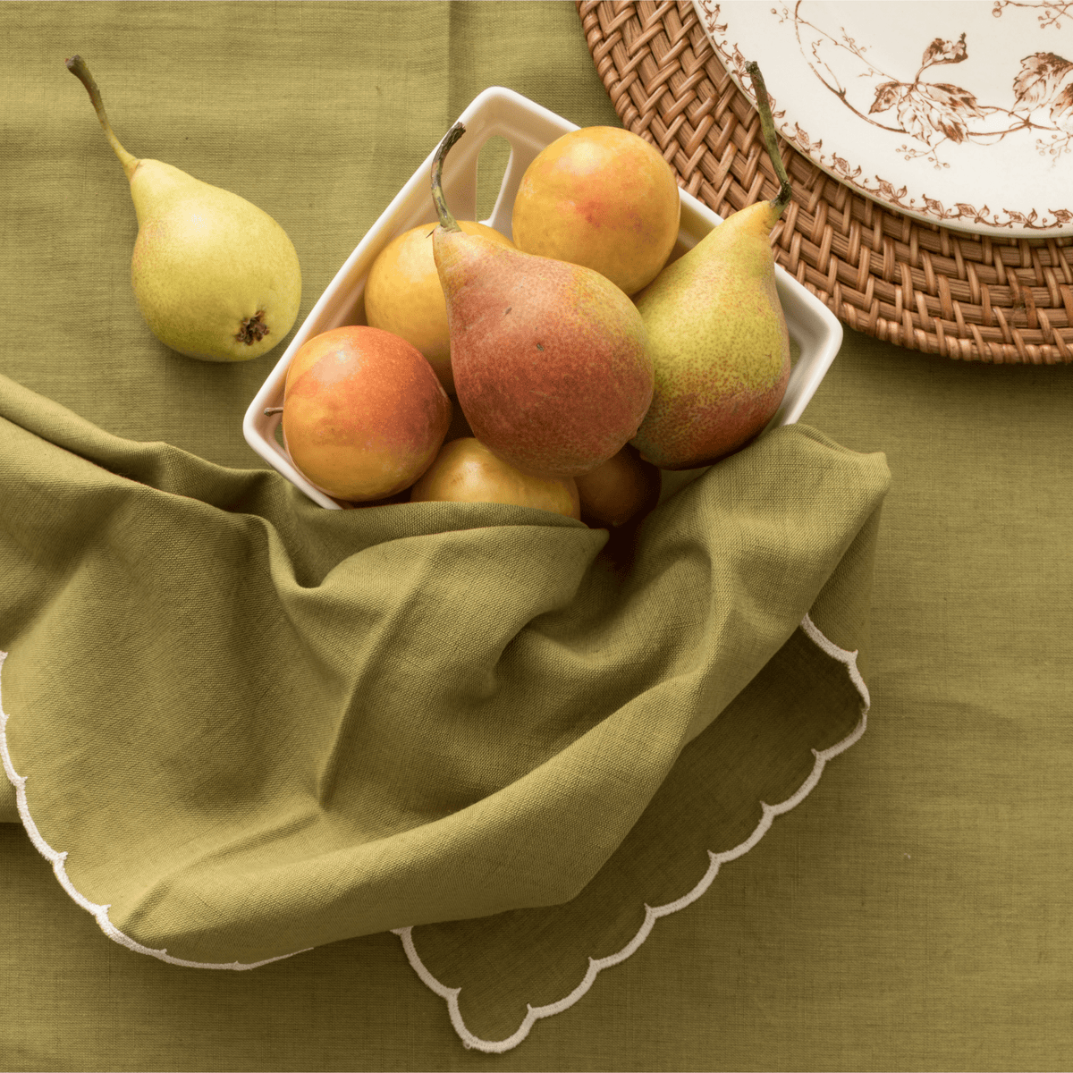 Olive scalloped napkin draped beside a bowl of pears on an olive tablecloth