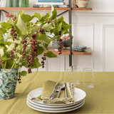 Olive scalloped napkins on stacked white plates with silverware on an olive tablecloth