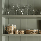 Be Home glass pitcher and matching tumblers wrapped in handwoven seagrass on a green shelf with glass vases.