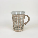 Be Home clear glass pitcher wrapped in handwoven natural seagrass with a sturdy handle and pour spout.