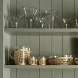 Be Home glass pitcher and matching tumblers wrapped in handwoven seagrass on a green shelf with glass vases.