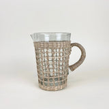 Be Home clear glass pitcher wrapped in handwoven natural seagrass with a sturdy handle and pour spout.