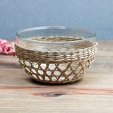 Be Home seagrass cage bowl with a clear glass insert, featuring a hand-woven natural fiber design on a table.