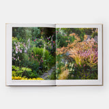 Calimia Home The Seasonal Gardener book open to a spread showing a lush planted border along a garden path.