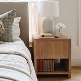 Sevilla Nightstand in natural oak by Grove & Anchor, styled beside a bed with a table lamp and books, exclusive to Calimia Home