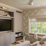A styled living room interior featuring a cream-colored curved sofa with patterned throw pillows, a matching upholstered ottoman, a built-in TV cabinet, and a window with a built-in window seat.