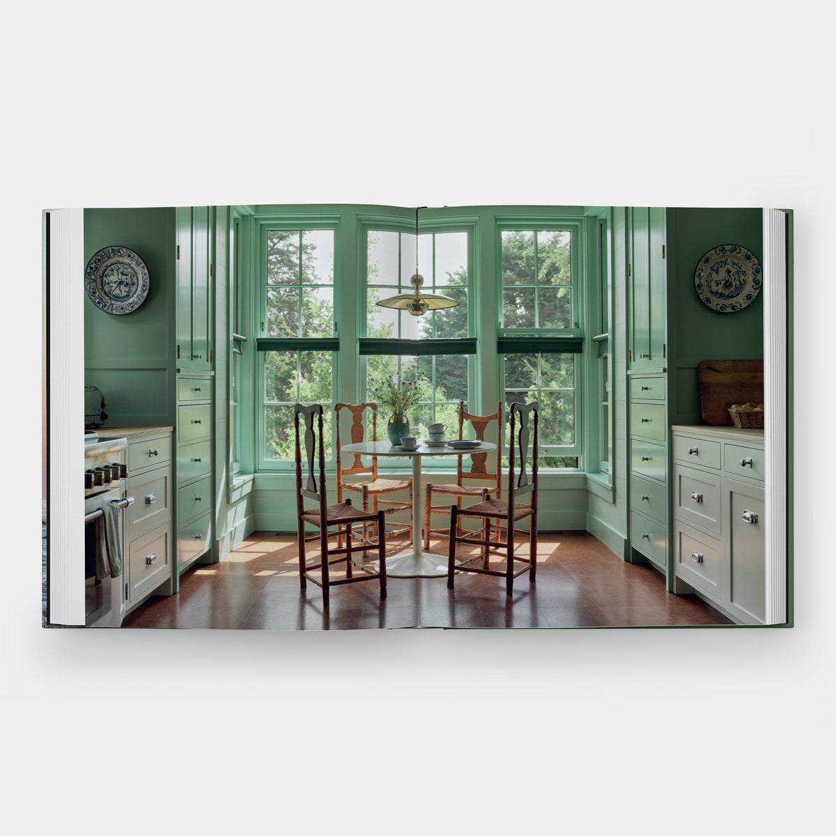 Calimia Home Summer by the Sea book open to a spread showing a green-painted cottage kitchen with a round dining table.