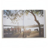 Calimia Home Sunday Suppers cookbook open to a page featuring a sunlit city picnic scene by the river