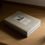 Calimia Home Sunday Suppers linen-bound cookbook with a neutral beige cover resting on a wooden surface.