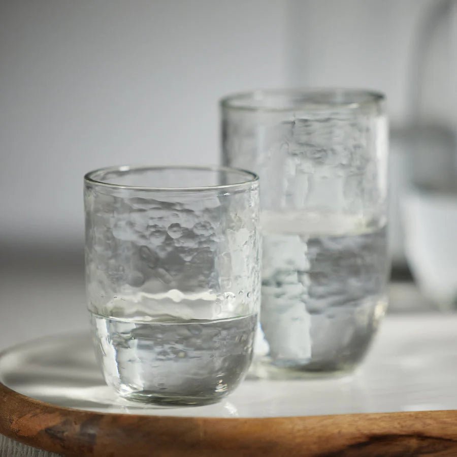 Two Tabou hammered glass tumblers on a wooden surface