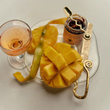 A scored mango and coupe glass share a plate with the Flamingo Estate Salsa Macha Chile Crisp jar and a gold spoon, hinting at sweet-meets-spicy pairings.