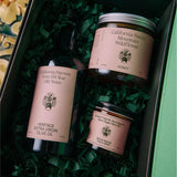 Inside the open Chef's Kiss gift box, the honey jar, olive oil bottle, and salsa macha chile crisp nestle in green crinkle paper from Calimia Home Shop.
