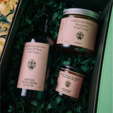 Inside the open Chef's Kiss gift box, the honey jar, olive oil bottle, and salsa macha chile crisp nestle in green crinkle paper from Calimia Home Shop.